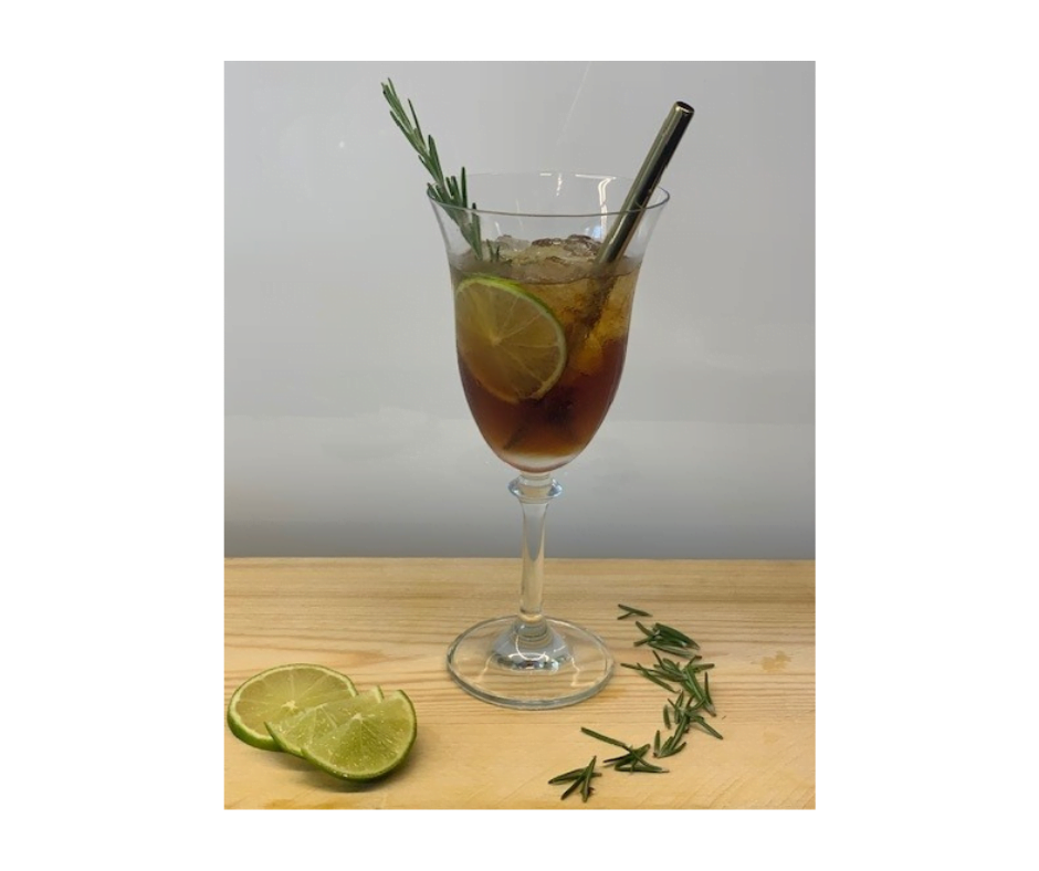 Een sfeervol glas gevuld met crushed ice en Conviv Bianco. Het geheel is gegarneerd met een takje rozemarijn en een goudkleurig rietje. Op de voorgrond liggen een paar schijfjes limoen en wat rozemarijn.